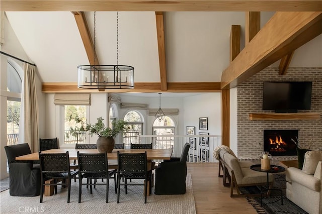 dining area featuring hardwood / wood-style floors, a brick fireplace, high vaulted ceiling, a chandelier, and beamed ceiling