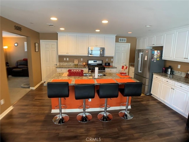 kitchen with white cabinetry, appliances with stainless steel finishes, stone countertops, and an island with sink