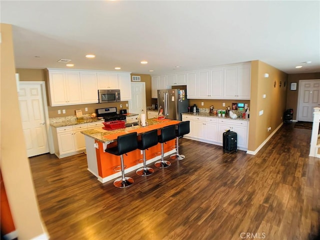 kitchen with a kitchen island with sink, stainless steel appliances, a kitchen breakfast bar, white cabinets, and dark hardwood / wood-style flooring