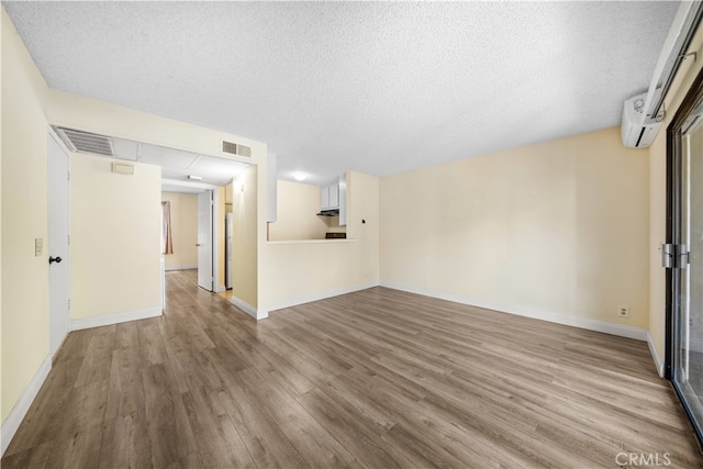 unfurnished living room featuring an AC wall unit, a textured ceiling, and light hardwood / wood-style flooring