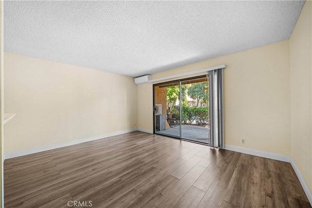 spare room featuring a wall unit AC, a textured ceiling, and hardwood / wood-style flooring