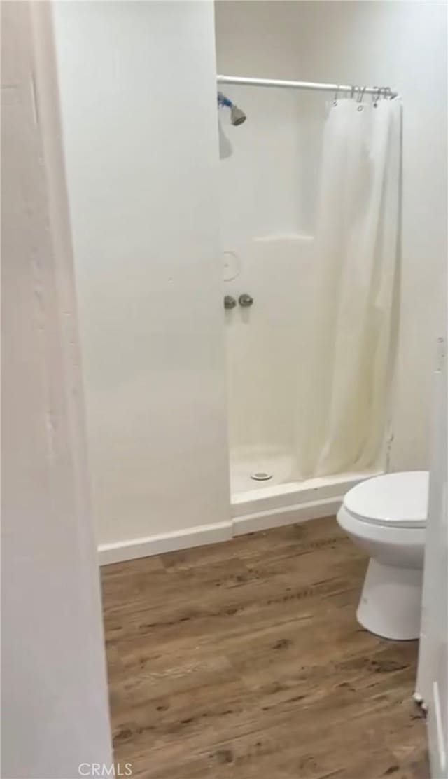 bathroom with toilet, a shower with curtain, and wood-type flooring