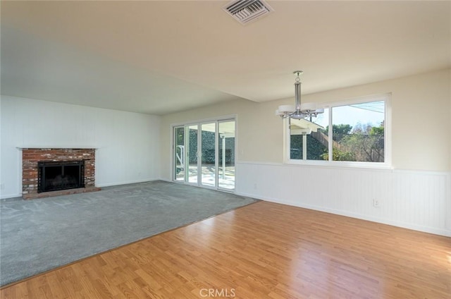 unfurnished living room featuring a brick fireplace, light hardwood / wood-style flooring, and a chandelier