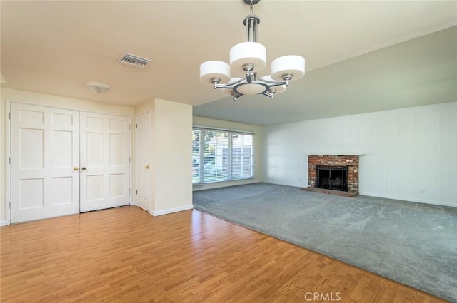 unfurnished living room with a brick fireplace, hardwood / wood-style flooring, and a notable chandelier