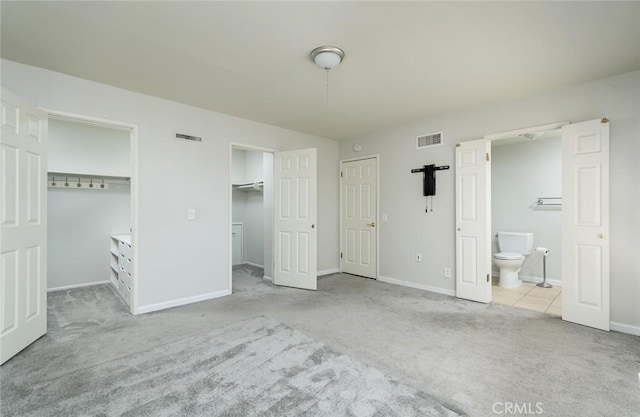 unfurnished bedroom with two closets, light colored carpet, and ensuite bath