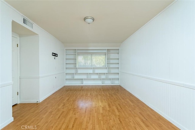 empty room with built in shelves and light wood-type flooring