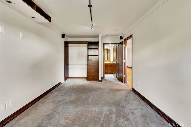 unfurnished bedroom featuring crown molding, rail lighting, light carpet, and ensuite bathroom