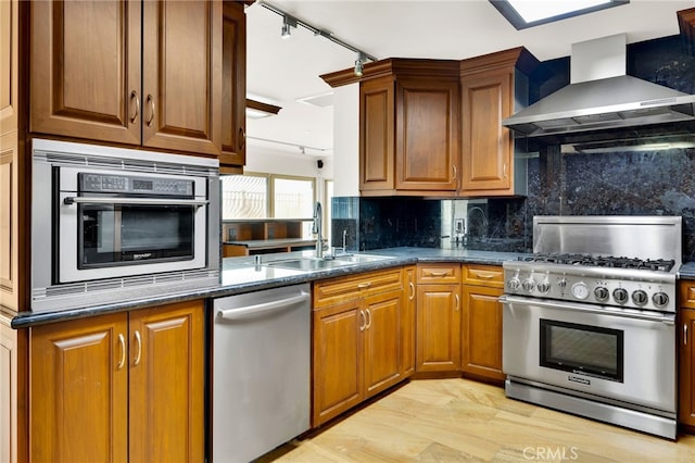 kitchen featuring appliances with stainless steel finishes, sink, decorative backsplash, wall chimney range hood, and light hardwood / wood-style flooring