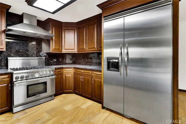 kitchen with tasteful backsplash, wall chimney range hood, light hardwood / wood-style flooring, and appliances with stainless steel finishes