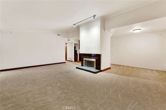 unfurnished living room featuring rail lighting, vaulted ceiling, light colored carpet, and crown molding