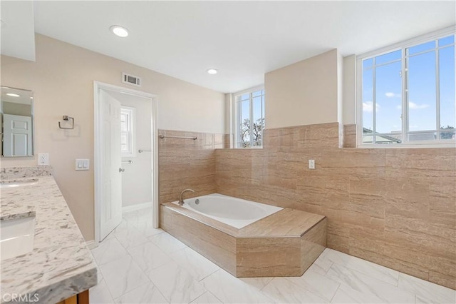 bathroom featuring tiled tub, vanity, and tile walls