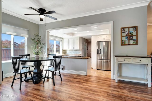 dining space with plenty of natural light, a tray ceiling, crown molding, and light wood-type flooring