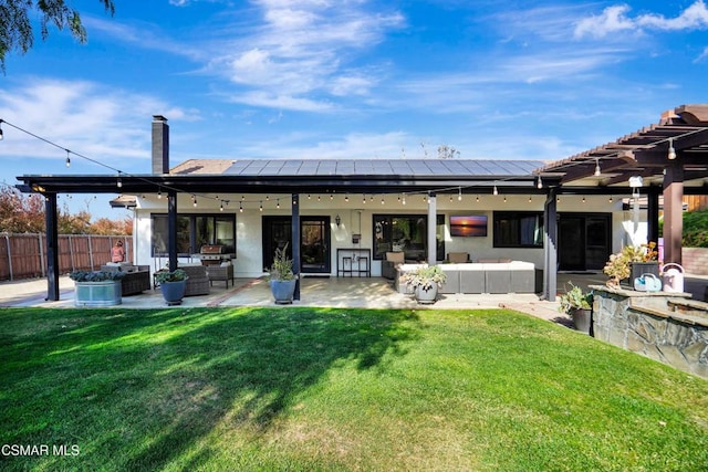 rear view of property with a patio area, outdoor lounge area, a lawn, and solar panels