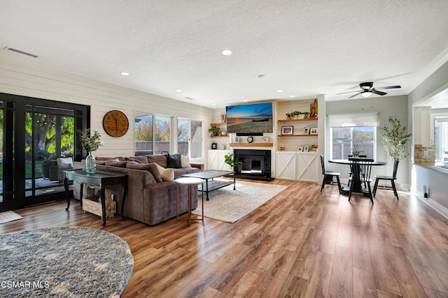 living room featuring a textured ceiling, ceiling fan, wood-type flooring, and a tile fireplace