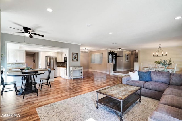 living room featuring crown molding, light wood-type flooring, and ceiling fan with notable chandelier