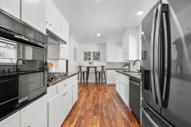 kitchen with stainless steel appliances, dark hardwood / wood-style floors, dark stone countertops, wall chimney range hood, and white cabinets