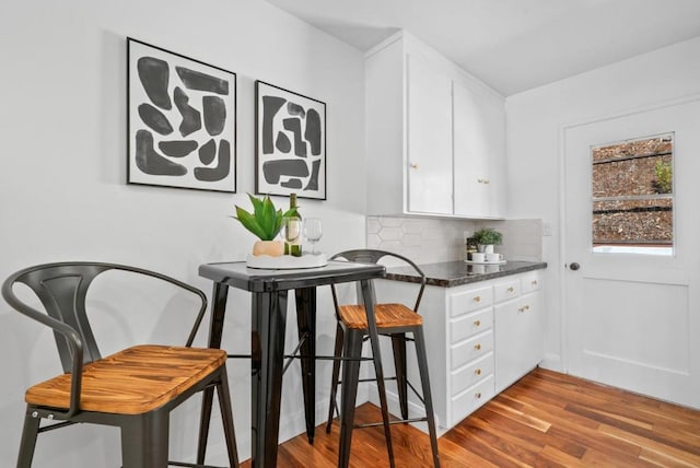 kitchen with tasteful backsplash, dark stone countertops, light hardwood / wood-style flooring, a kitchen breakfast bar, and white cabinets