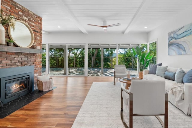 living room with a brick fireplace, a healthy amount of sunlight, beam ceiling, and wood-type flooring