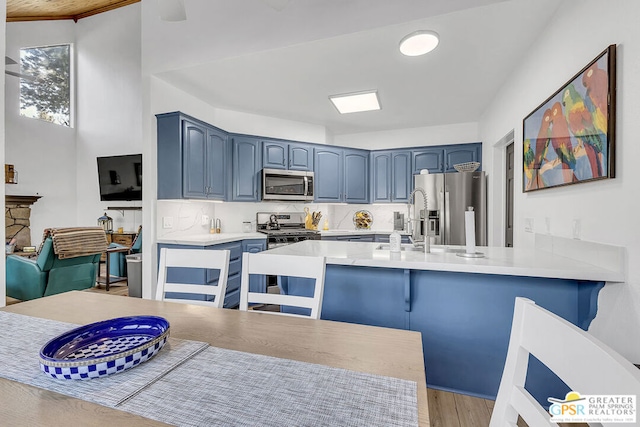 kitchen with kitchen peninsula, appliances with stainless steel finishes, light hardwood / wood-style flooring, and blue cabinetry