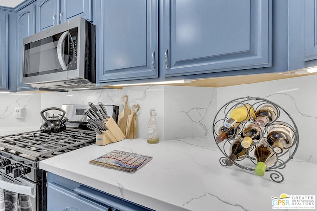 kitchen featuring stainless steel appliances, backsplash, blue cabinetry, and light stone countertops