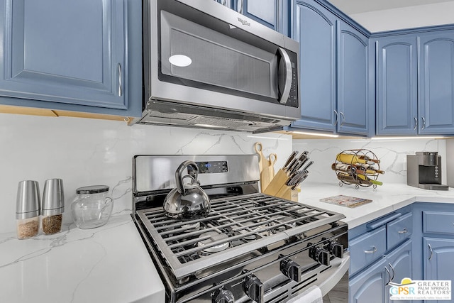 kitchen with appliances with stainless steel finishes, blue cabinets, tasteful backsplash, and light stone counters