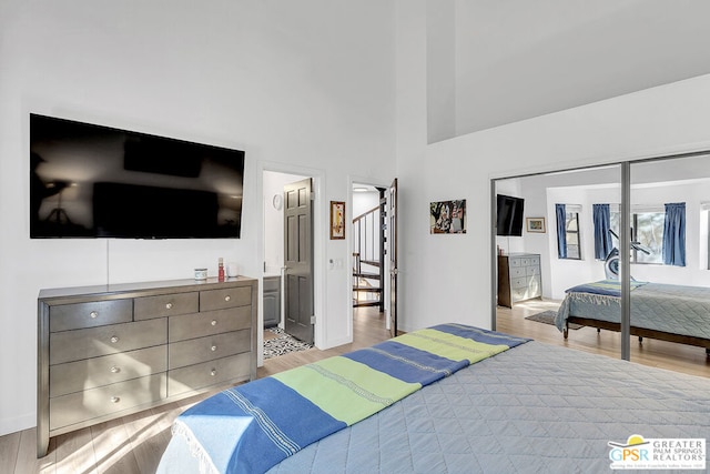 bedroom featuring light wood-type flooring, a closet, a high ceiling, and ensuite bath