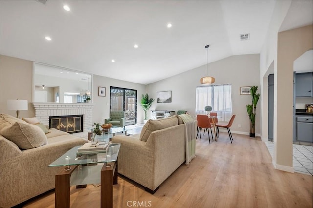 living room featuring vaulted ceiling, a fireplace, and light hardwood / wood-style flooring