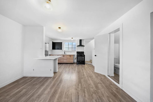 kitchen with kitchen peninsula, light hardwood / wood-style flooring, wall chimney range hood, black range with gas cooktop, and stainless steel refrigerator