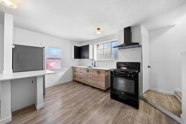 kitchen featuring wall chimney range hood, light hardwood / wood-style floors, sink, black gas range, and stainless steel refrigerator