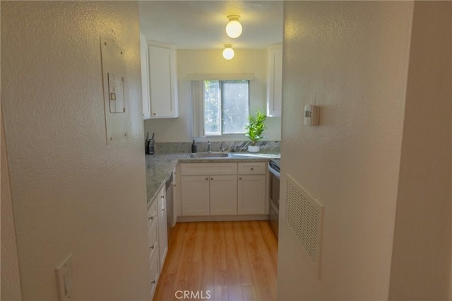 kitchen with sink, white cabinetry, light wood-type flooring, range with electric cooktop, and light stone counters