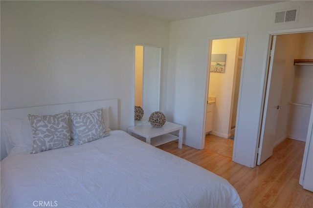 bedroom with a spacious closet, ensuite bathroom, and light hardwood / wood-style floors