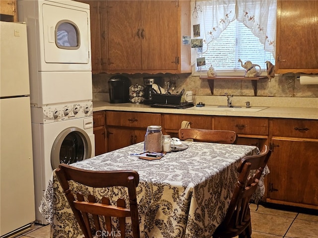 kitchen featuring light tile patterned floors, stacked washer and dryer, sink, and white fridge