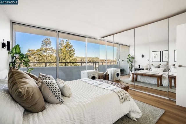 bedroom with a wall of windows, wood-type flooring, separate washer and dryer, and multiple windows