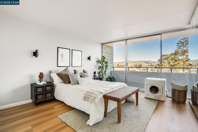 bedroom with floor to ceiling windows, a mountain view, wood-type flooring, and access to outside