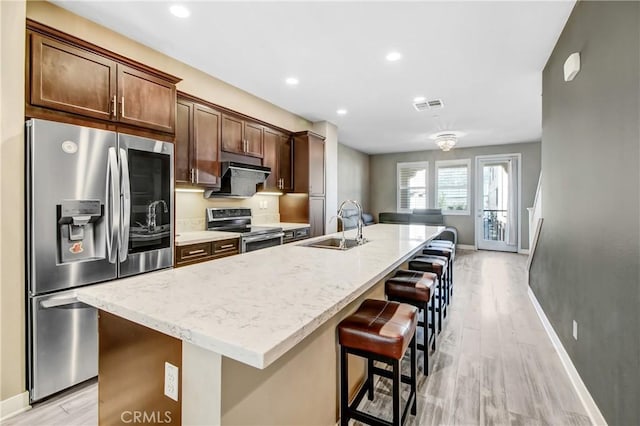 kitchen with light hardwood / wood-style floors, sink, a center island with sink, and stainless steel appliances