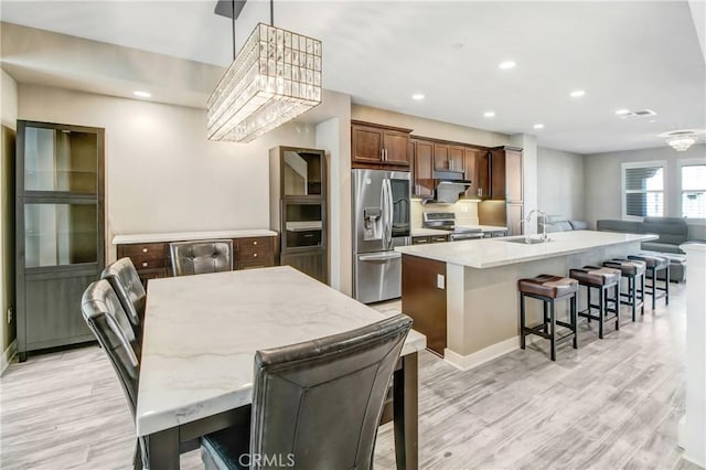 kitchen with a center island with sink, appliances with stainless steel finishes, a kitchen breakfast bar, pendant lighting, and sink