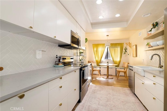 kitchen with white cabinets, stainless steel appliances, tasteful backsplash, hanging light fixtures, and a tray ceiling