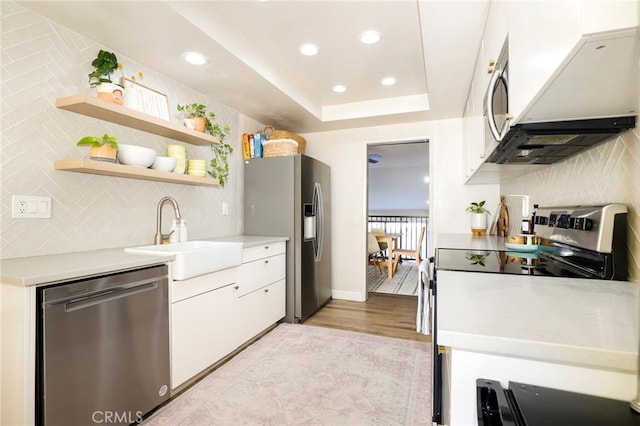 kitchen featuring a raised ceiling, sink, white cabinetry, light hardwood / wood-style floors, and stainless steel appliances