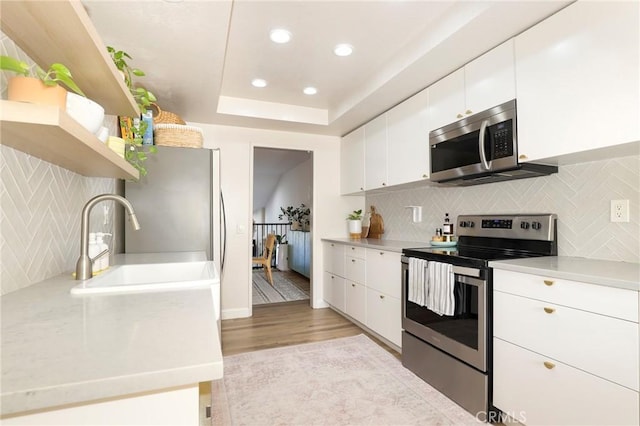 kitchen featuring backsplash, white cabinets, light hardwood / wood-style flooring, and appliances with stainless steel finishes