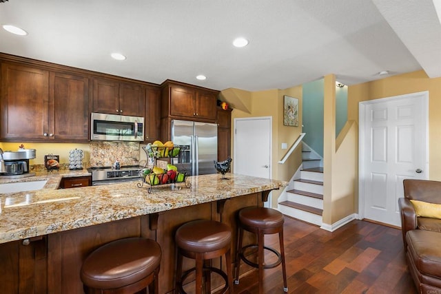 kitchen with dark hardwood / wood-style flooring, backsplash, light stone countertops, a kitchen bar, and stainless steel appliances