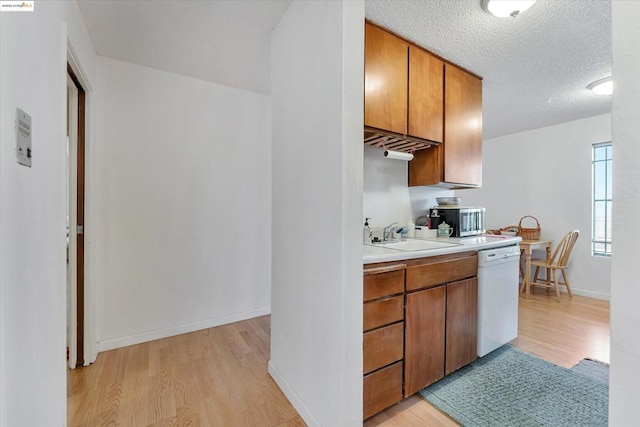 kitchen with light wood-type flooring, a textured ceiling, dishwasher, and sink