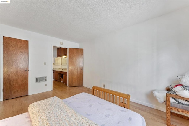 bedroom featuring a textured ceiling, connected bathroom, and light hardwood / wood-style floors