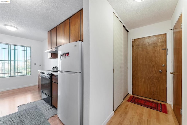 kitchen with electric stove, a textured ceiling, white fridge, and light hardwood / wood-style floors