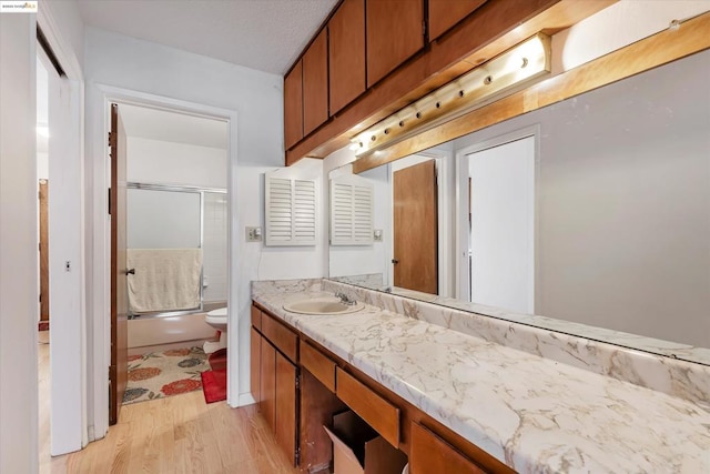 bathroom featuring hardwood / wood-style flooring, vanity, and shower / bath combination with glass door