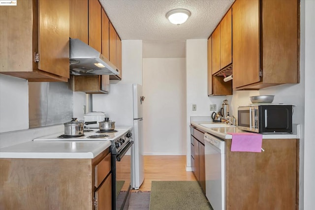 kitchen with a textured ceiling, sink, light hardwood / wood-style flooring, and white appliances