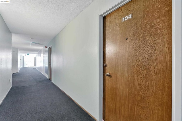 hallway featuring a textured ceiling and dark carpet