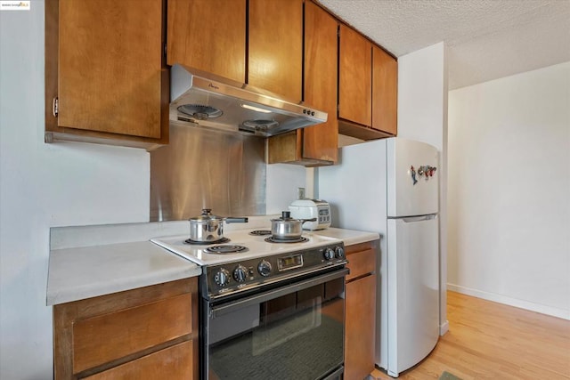 kitchen with black range with electric stovetop, white fridge, a textured ceiling, and light hardwood / wood-style flooring