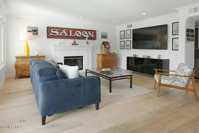 living room with a brick fireplace, light hardwood / wood-style floors, and crown molding