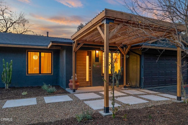 view of front of house featuring roof with shingles, an attached garage, and stucco siding