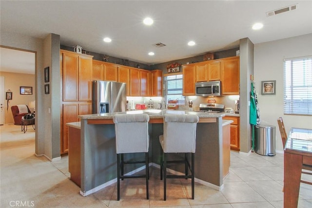 kitchen with light tile patterned flooring, appliances with stainless steel finishes, a center island with sink, and a kitchen breakfast bar